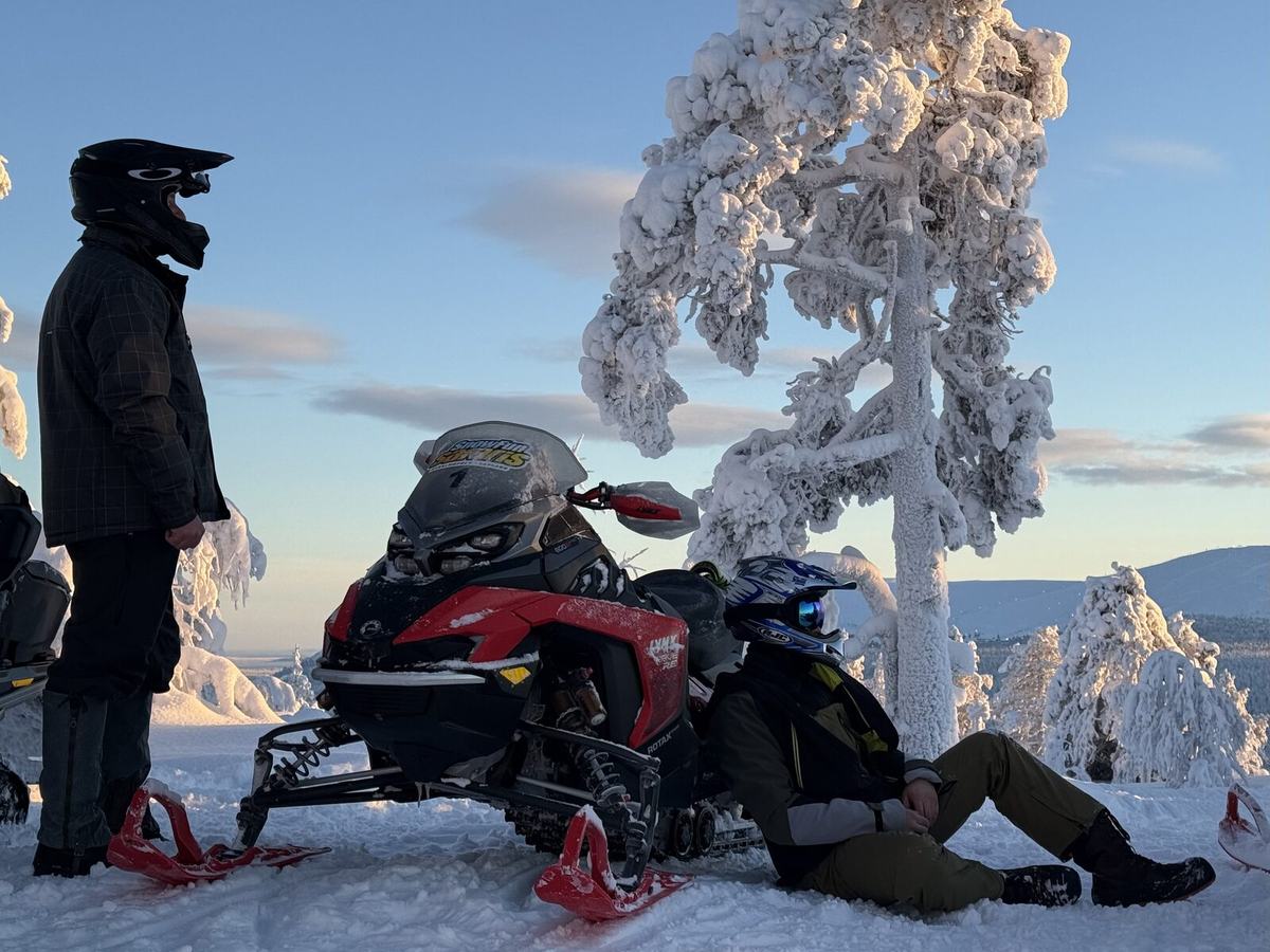 Zwei Personen machen eine Pause am Schneemobil im Schnee